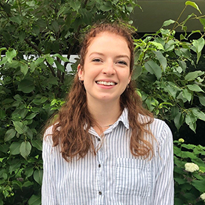 Courtney Wolfe smiling and standing against green foliage outside the Fishbowl office building