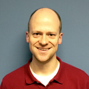 John Lundgren smiling while standing against a blue wall 